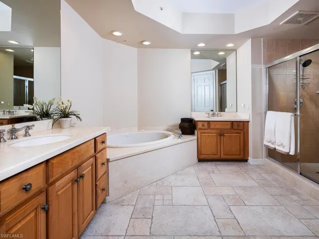 Bathroom with a stall shower, stone tile flooring, two vanities, a garden tub, and recessed lighting