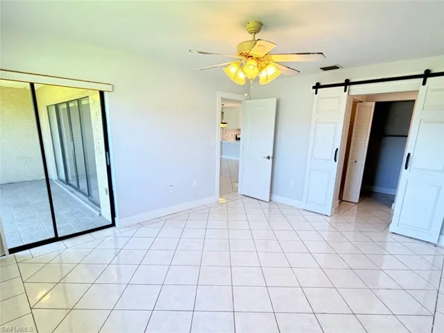 Neutral-toned room featuring large-format ceramic tile flooring, sliding glass door with a black frame, double barn-style doors with matte black hardware, and a ceiling-mounted light fixture with a fan