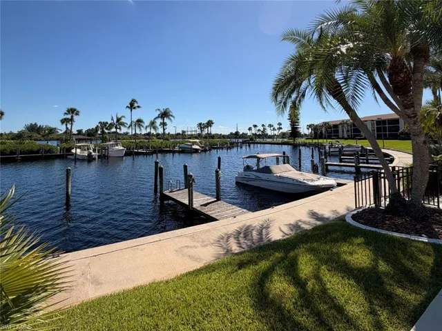 Waterfront canal featuring a private wood-plank dock, concrete seawall, manicured lawn, and mature palm trees