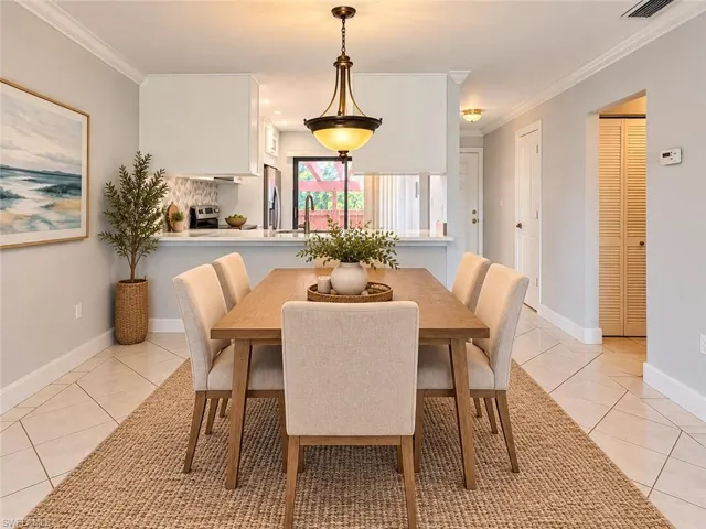 Virtually Staged  Dining area featuring diagonal-set tile flooring, crown molding, and a suspended metal-finish pendant light, with a pass-through opening to the kitchen area