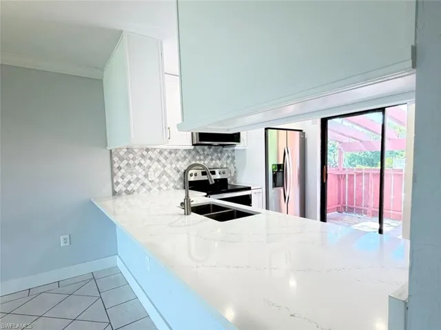 Kitchen featuring a white quartz countertop peninsula, mosaic tile backsplash, stainless steel appliances, and tile flooring