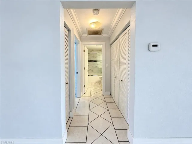 Hallway featuring diagonal tile flooring, crown molding, ceiling-mounted light fixture, and floor-to-ceiling louvered closet doors