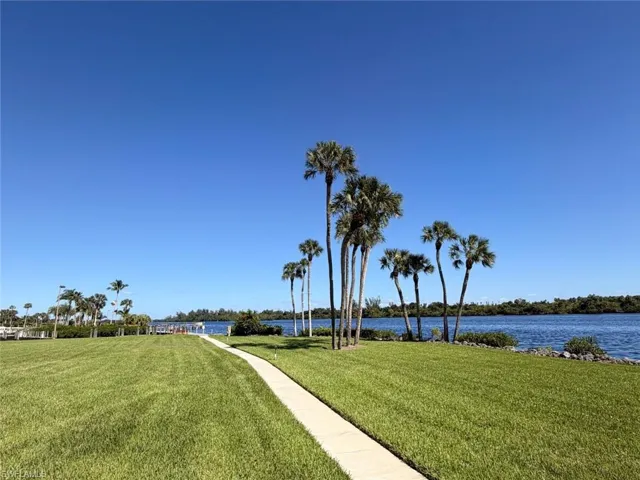 Waterfront grounds featuring mature palms, a concrete walkway, and expansive lawn space