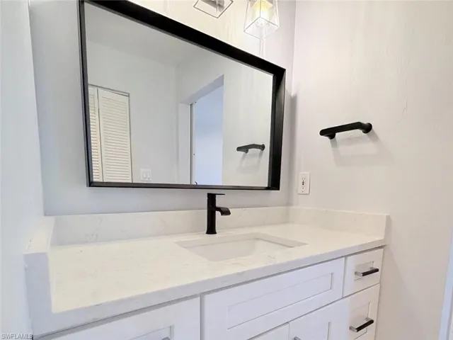White vanity featuring a stone countertop with an integrated basin, matte black faucet, rectangular framed mirror, and coordinating matte black hardware