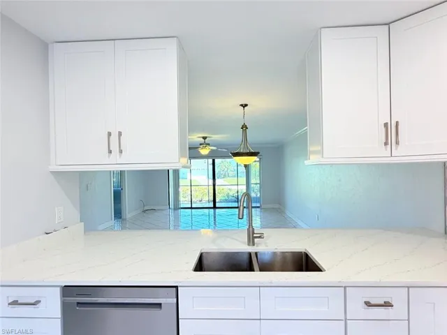 White shaker-style cabinetry, white stone-composite countertops with grey veining, stainless steel undermount double-basin sink with gooseneck faucet, and stainless steel dishwasher