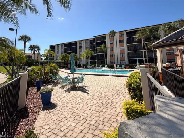 Community pool area featuring paver decking, metal perimeter fencing, and mature palm landscaping