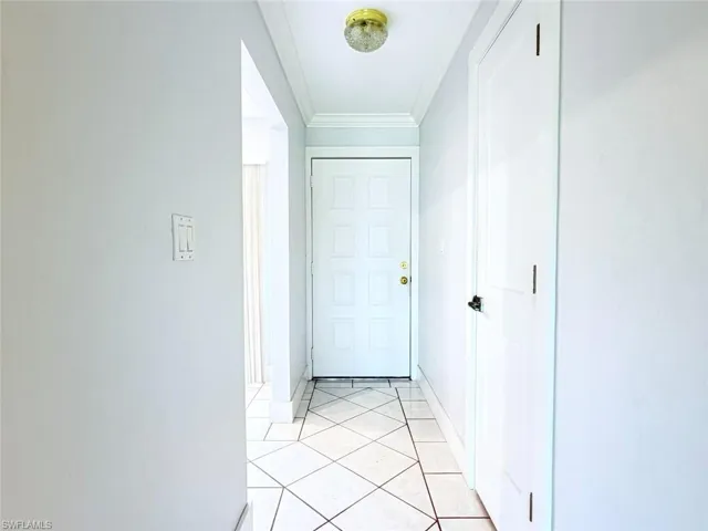 Entryway featuring tile flooring arranged in a diagonal pattern, white paneled door with brass-tone hardware, crown molding, and a flush-mount ceiling light fixture
