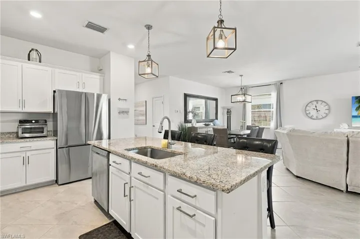 Kitchen featuring white cabinetry, granite, stainless steel appliances, a center island with bar seating, pendant lighting, and walk-in pantry
