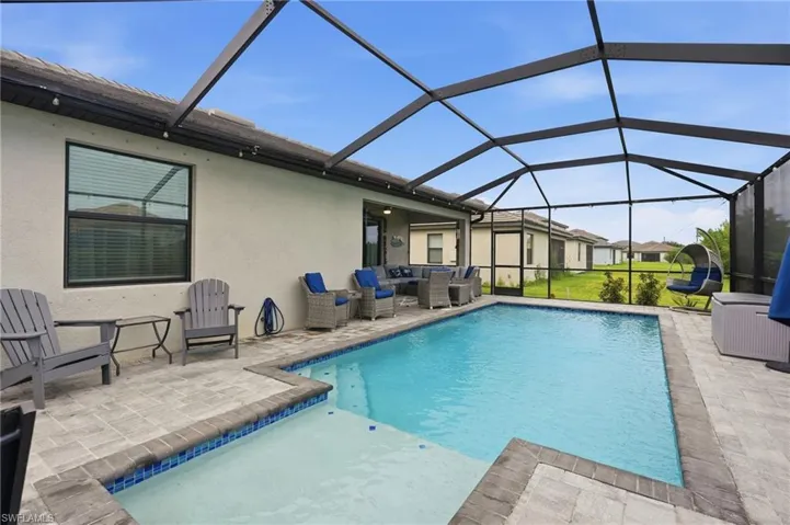 Screened-in outdoor living space featuring a custom swimming pool, integrated shallow lounging / tanning shelf, and extended paver patio and lanai.