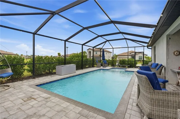 Screened-in outdoor living space featuring a custom swimming pool, integrated shallow lounging / tanning shelf, and extended paver patio and lanai.