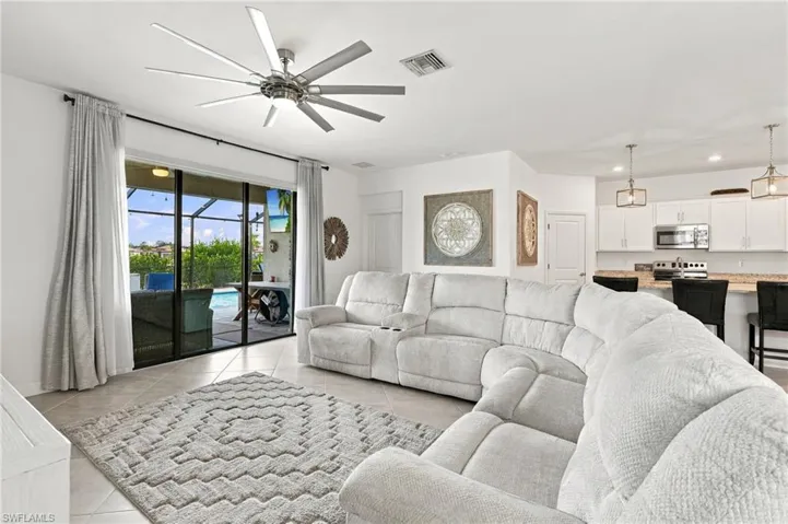 Spacious living area featuring tile flooring, a large ceiling fan, and sliding glass doors opening to a screened lanai