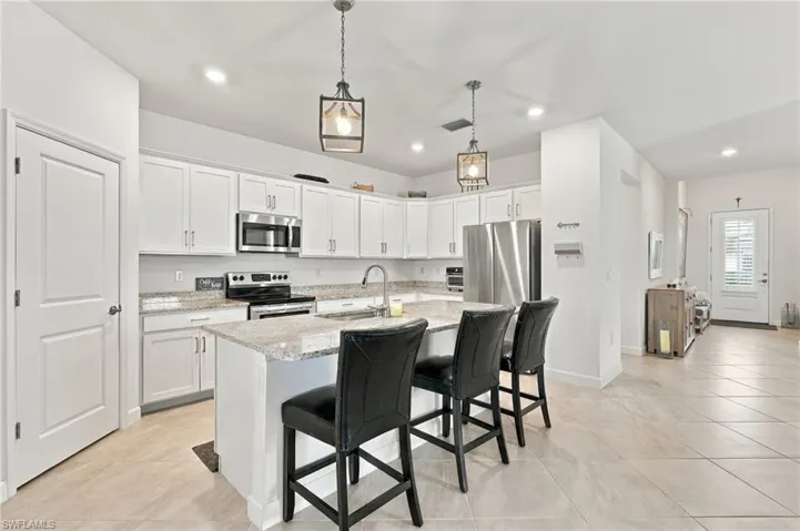 Kitchen featuring white cabinetry, granite, stainless steel appliances, a center island with bar seating, pendant lighting, and walk-in pantry
