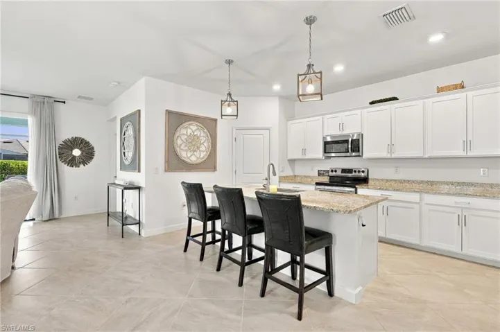Kitchen island with a built-in sink and pendant lighting, white cabinetry, integrated stainless steel appliances, and granite countertops