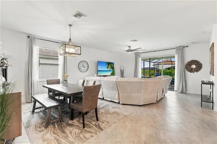 Open-concept living space featuring large format tile flooring, a dining area with a linear pendant light, a living area featuring slider with automated shade