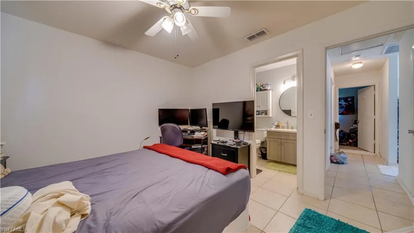 Bedroom featuring light tile patterned floors, ceiling fan, ensuite bathroom, and attic access
