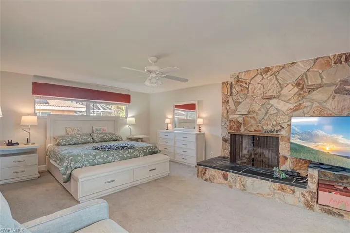 Bedroom with carpet, a stone fireplace, and a ceiling fan