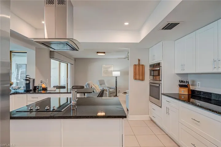 Kitchen featuring dark stone counters, island range hood, white cabinetry, and recessed lighting