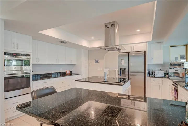 Kitchen featuring stainless steel appliances, dark stone counters, island exhaust hood, white cabinetry, and a center island