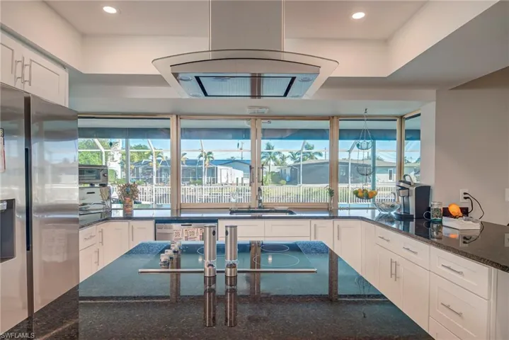 Kitchen with dark stone countertops, white cabinets, exhaust hood, stainless steel appliances, and recessed lighting