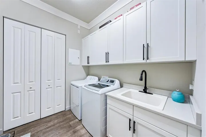 Laundry area with ornamental molding, sink, wood-type flooring, cabinets, and washer and dryer