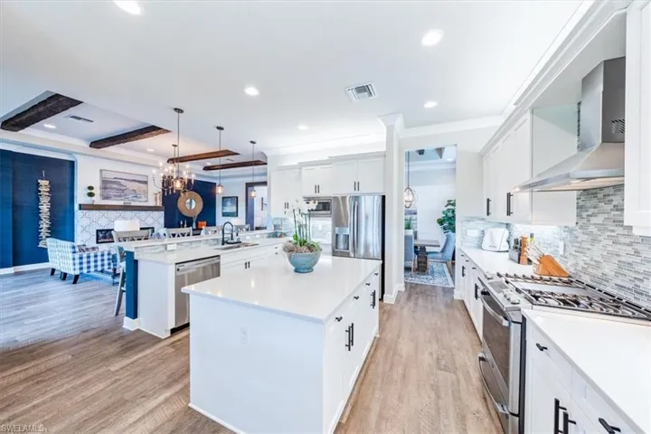 Kitchen featuring pendant lighting, stainless steel appliances, a center island, and wall chimney range hood