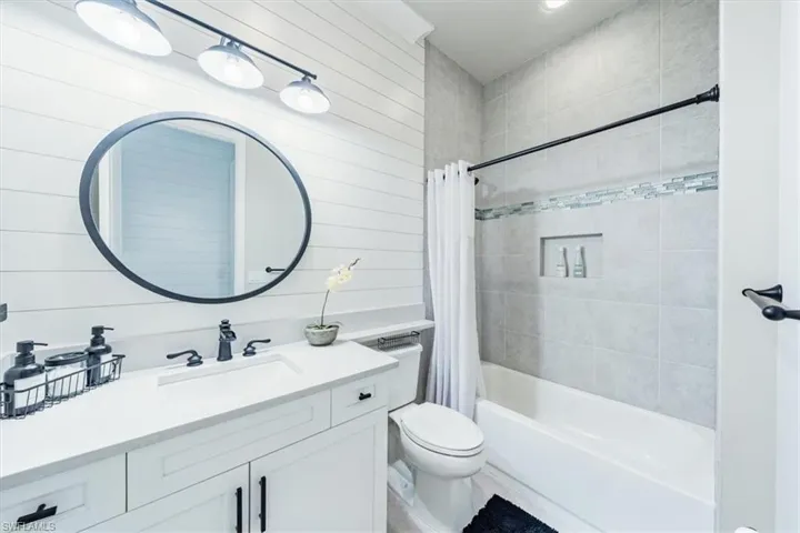 Full bathroom featuring vanity, wood walls, toilet, and shower / bathtub combination with curtain