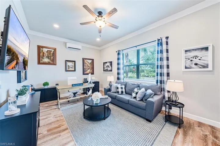 Living room with ceiling fan, ornamental molding, wood-type flooring, and a wall unit AC