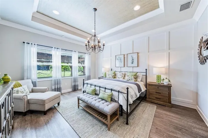 Bedroom featuring a raised ceiling, dark wood-type flooring, and a notable chandelier