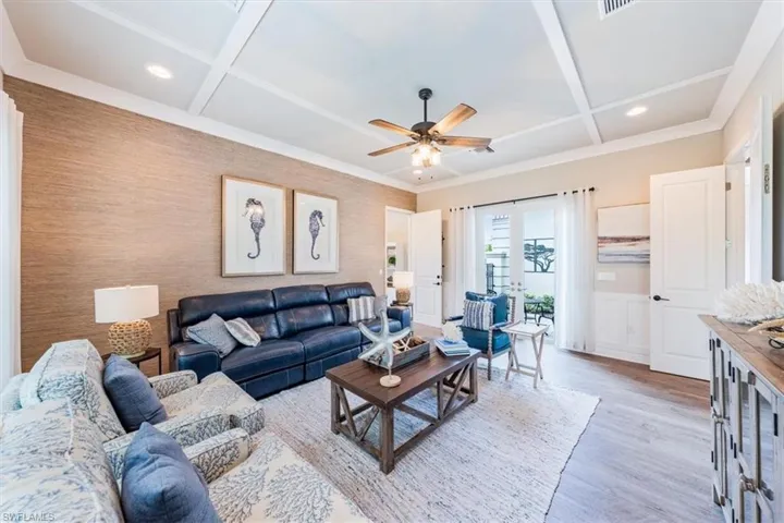 Living room with light wood-type flooring, beam ceiling, coffered ceiling, ceiling fan, and french doors