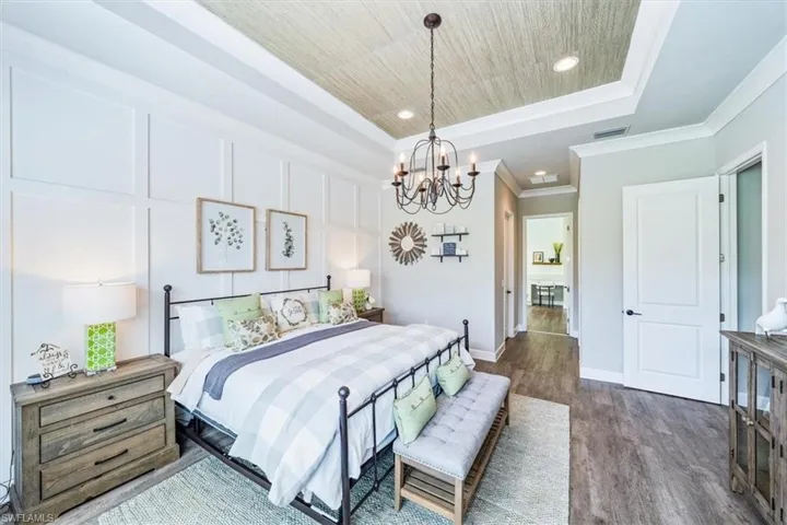 Bedroom with an inviting chandelier, a raised ceiling, and dark hardwood / wood-style floors
