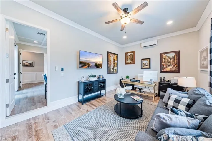 Living room featuring ceiling fan, light wood-type flooring, crown molding, and a wall unit AC