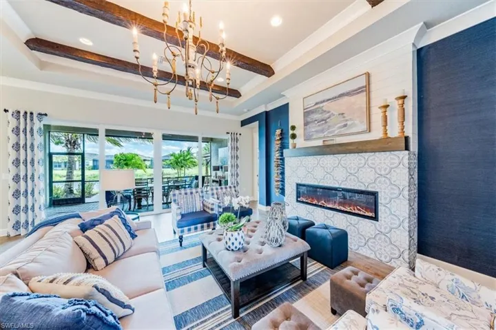 Living room featuring beam ceiling, a chandelier, hardwood / wood-style floors, and a stone fireplace