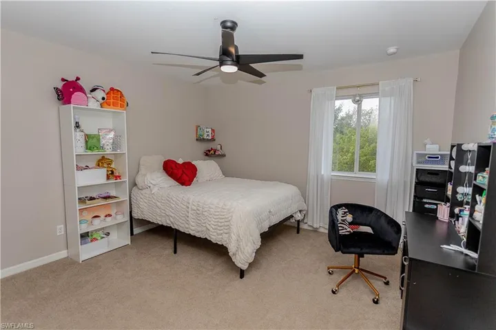 Bedroom with light colored carpet, ceiling fan, and a desk
