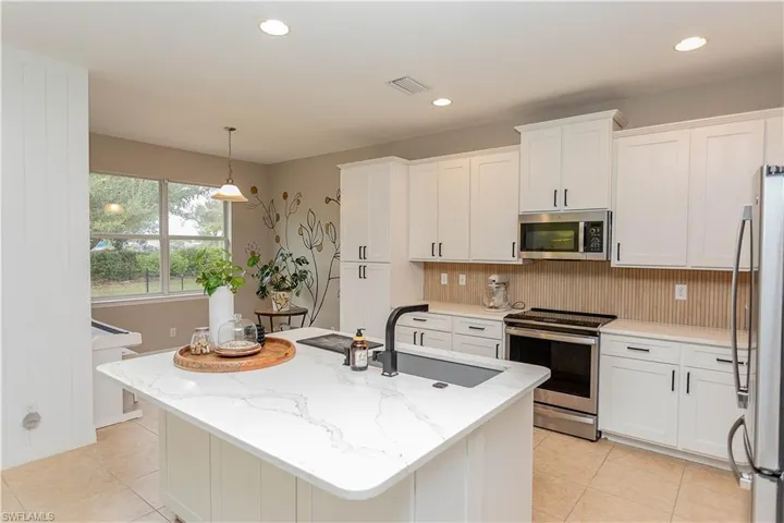 Kitchen with stainless steel appliances, white cabinets, and light stone counters