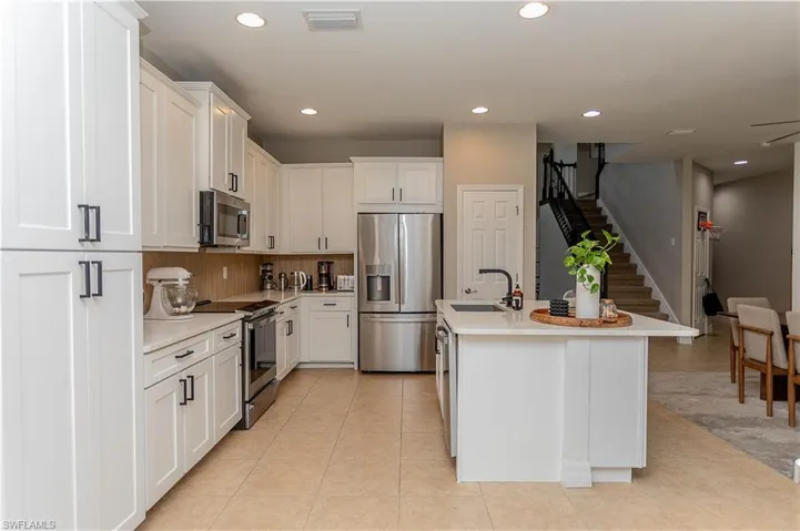 Kitchen featuring white cabinetry, stainless steel appliances, a center island with sink, recessed lighting, and light stone counters
