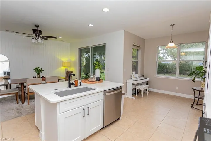 Kitchen featuring pendant lighting, stainless steel appliances, white cabinetry, light stone counters, and a kitchen island with sink