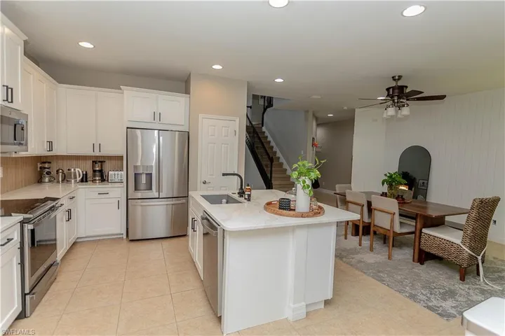 Kitchen with stainless steel appliances, a center island with sink, white cabinets, ceiling fan, and light stone countertops