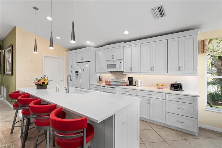 Kitchen with a kitchen breakfast bar, white appliances, a sink, an island with sink, and visible vents