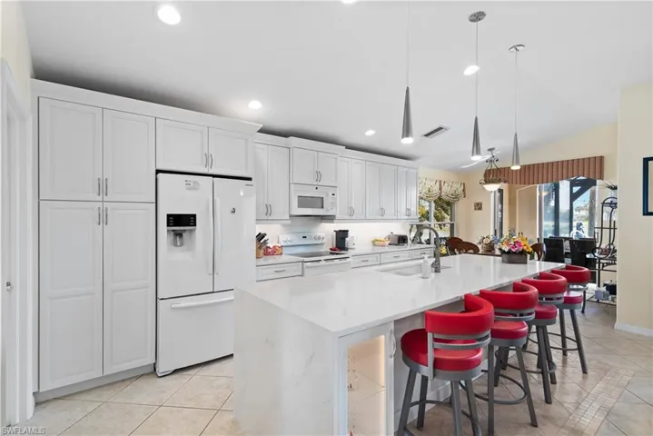 Kitchen with light tile patterned flooring, visible vents, white appliances, white cabinetry, and a sink