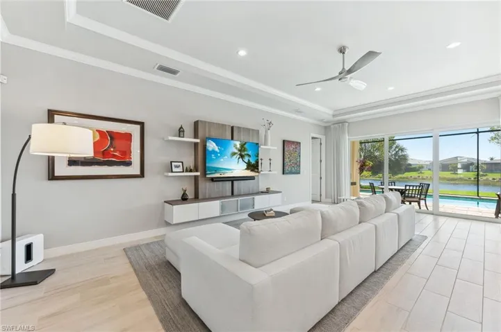 Living room with a tray ceiling, visible vents, ceiling fan, and crown molding