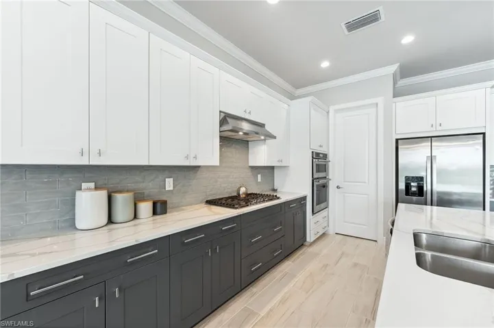 Kitchen with visible vents, stainless steel appliances, under cabinet range hood, white cabinetry, and crown molding