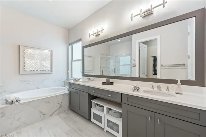 Bathroom featuring double vanity, a bath, a marble finish shower, and a sink