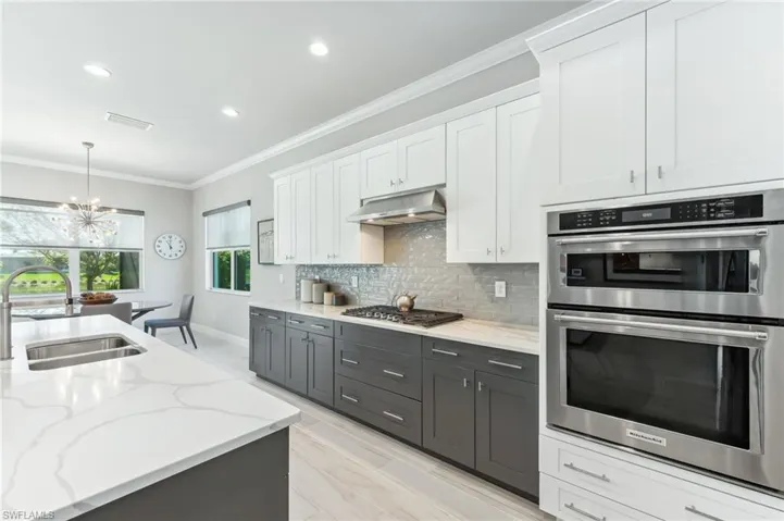 Kitchen featuring backsplash, under cabinet range hood, ornamental molding, appliances with stainless steel finishes, and a sink