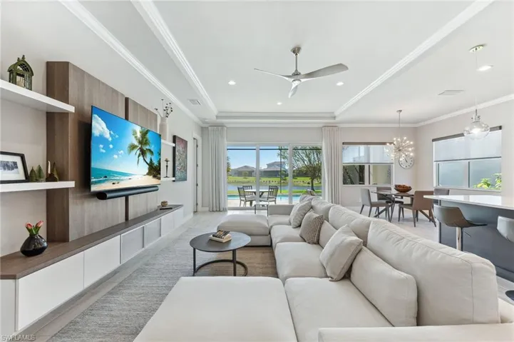 Living room featuring visible vents, crown molding, recessed lighting, ceiling fan with notable chandelier, and a raised ceiling