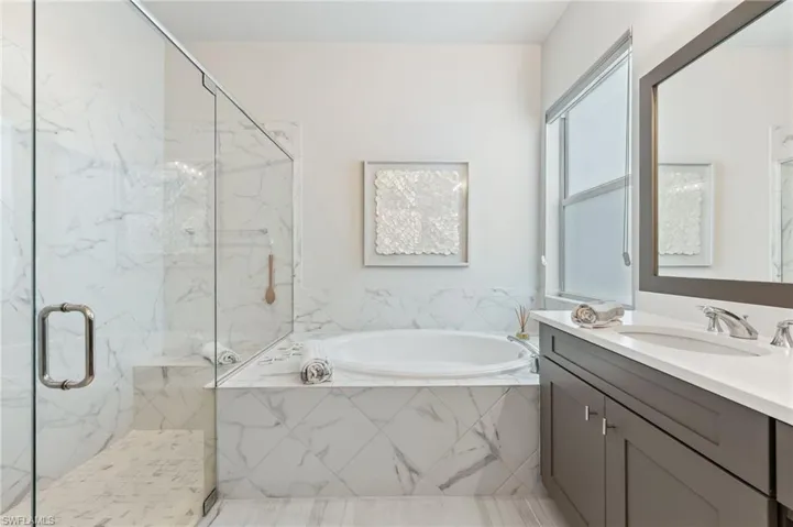 Full bath featuring vanity, a bath, and a marble finish shower