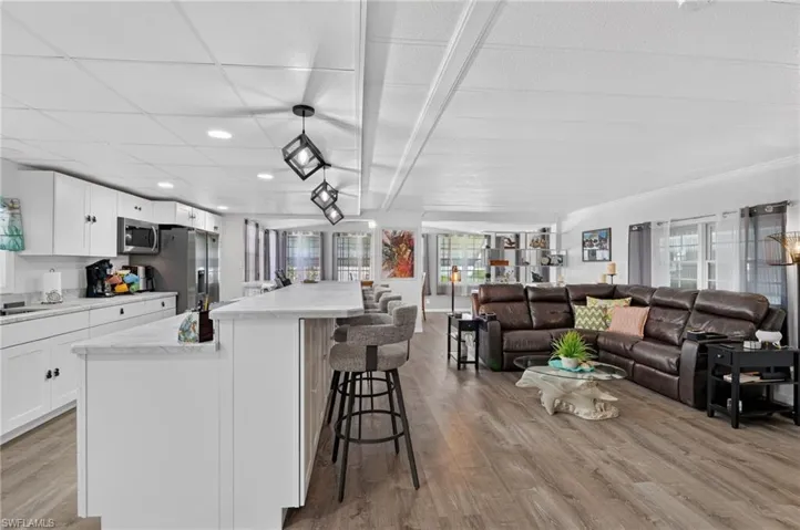 Spacious interior featuring wood-finish flooring, white cabinetry, stainless steel appliances, and a large kitchen island with counter seating