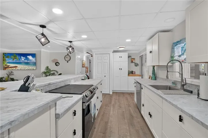Kitchen featuring light wood-finish flooring, white cabinetry, a built-in electric range, a stainless steel sink with a gooseneck faucet, and recessed lighting