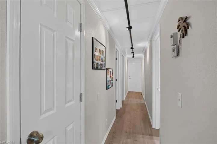 Hallway featuring wood-finish flooring, crisp white trim, track lighting, and panel doors