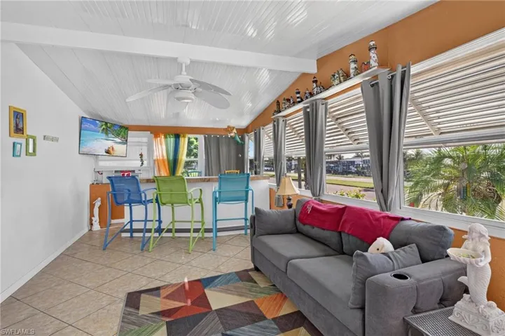 Vaulted white planked ceiling with a ceiling fan, tiled flooring, expansive windows with horizontal blinds, and a built-in bar with a countertop
