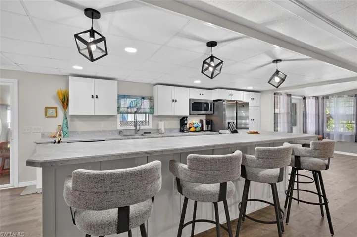 Kitchen island with seating, white cabinetry, integrated stainless steel appliances, recessed lighting, and geometric pendant light fixtures